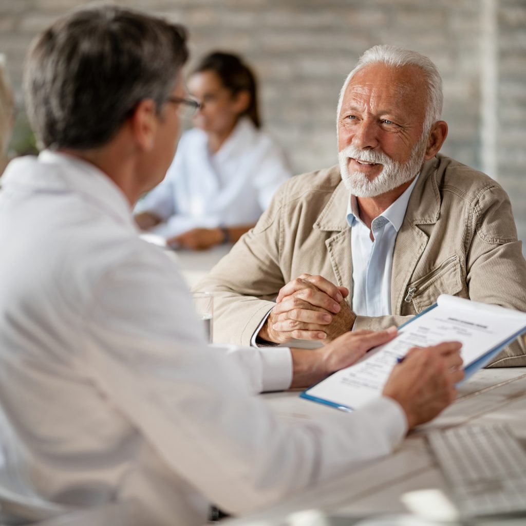 Happy mature man having consultations with a doctor about health insurance policy during a meeting at clinic.